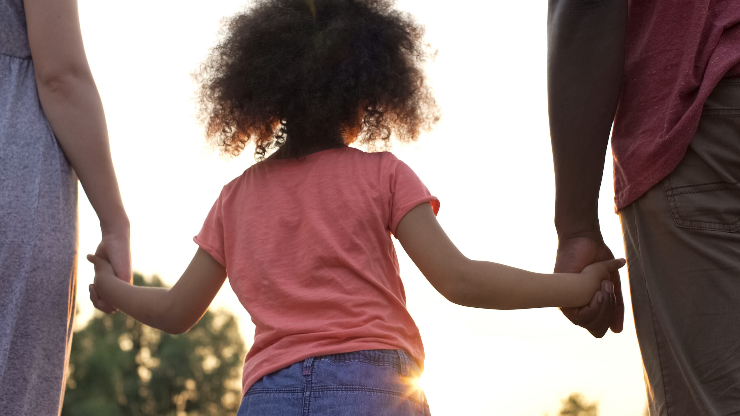 Curly-haired girly holding her mother and father hands, happiness in family